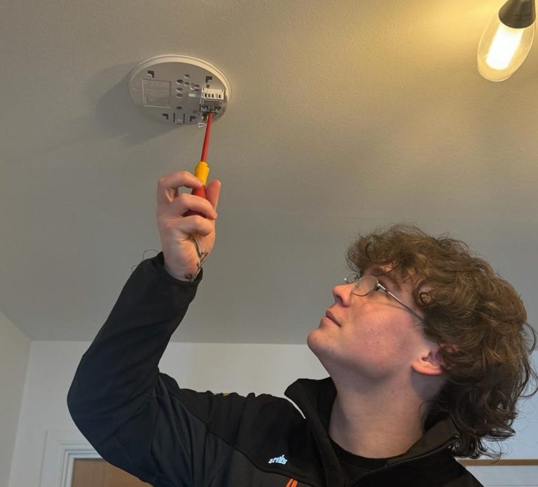 KF Watson engineer working from a ladder installing ceiling mounted smoke detector